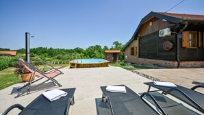 Un espace piscine doté de chaises longues et d’un jacuzzi, entouré d’une maison en bois avec un mur en pierre.