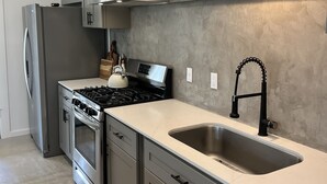 A modern kitchen with stainless steel appliances, grey cabinets, and a black pendant light. - Secluded cottage nestled in the Homochitto National Forest. Fireplace & pond. (Crosby)