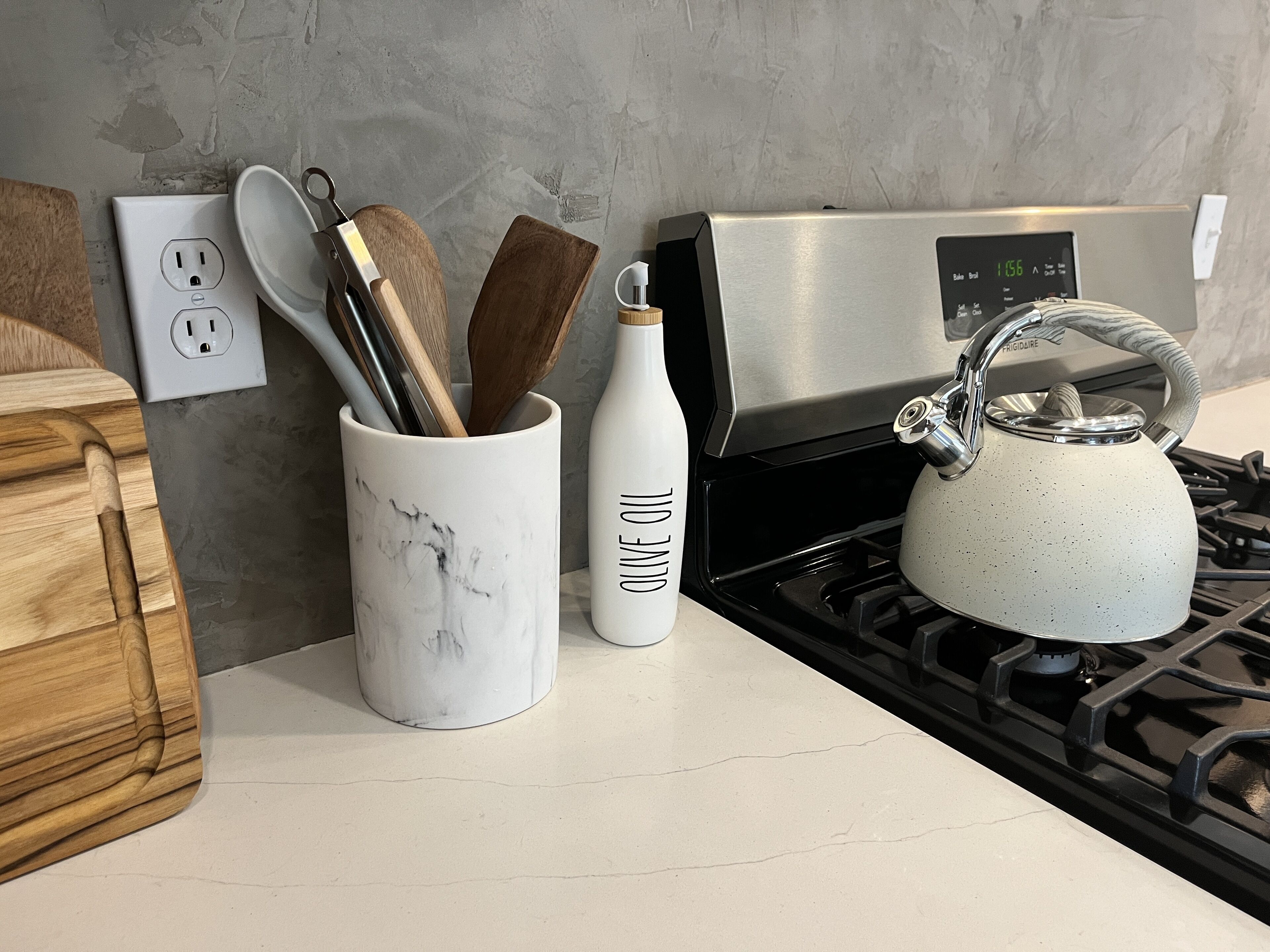 A kitchen counter with a marble mug, a white bottle labeled "Olive Oil," and a kettle.