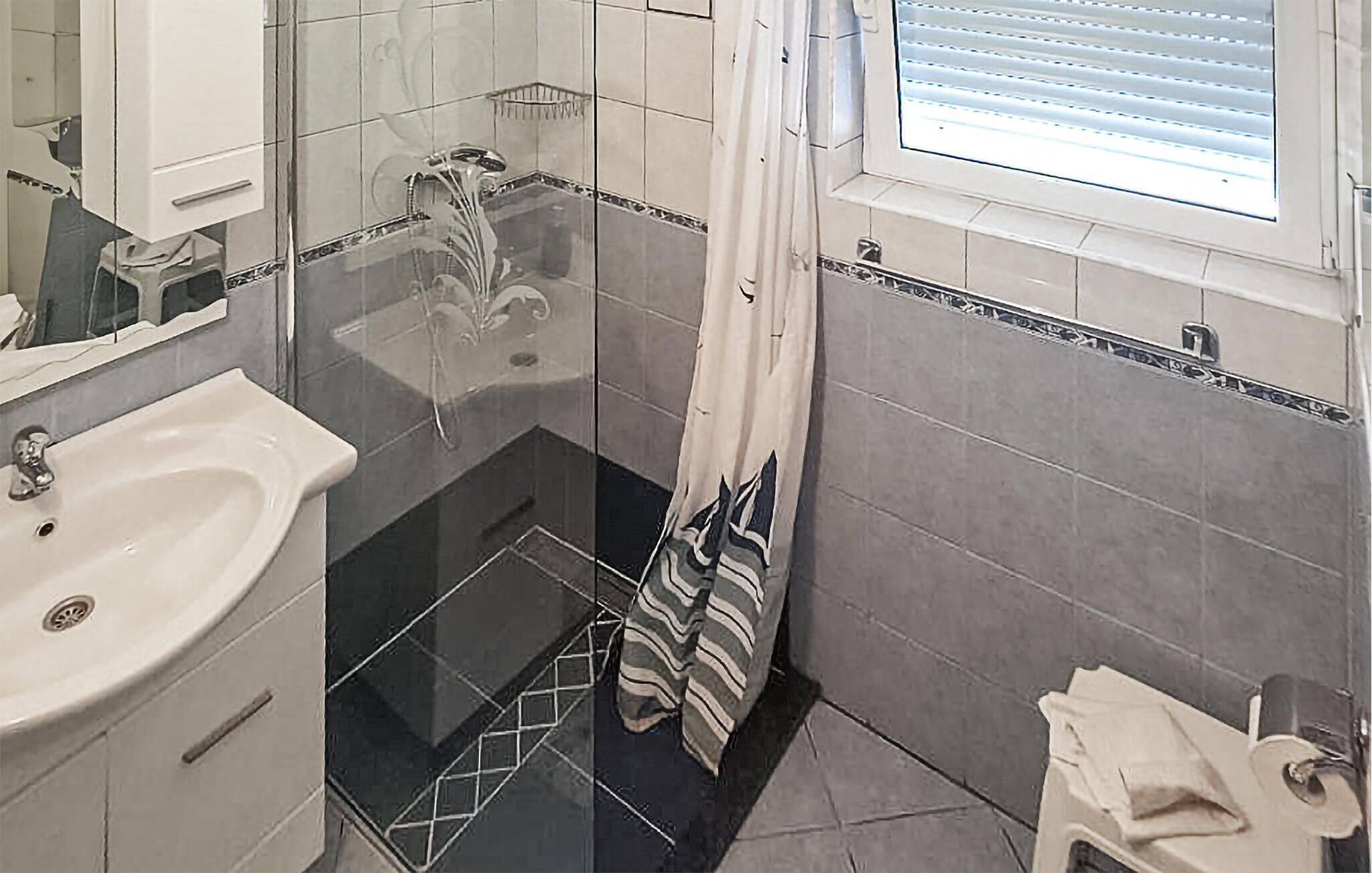A bathroom with a sink, shower, and window.