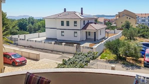A two-story house with a tiled roof, surrounded by a fence and greenery.