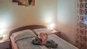 A neatly made bed with a heart-shaped towel and a blanket, two bedside lamps, and a wall with a painting.