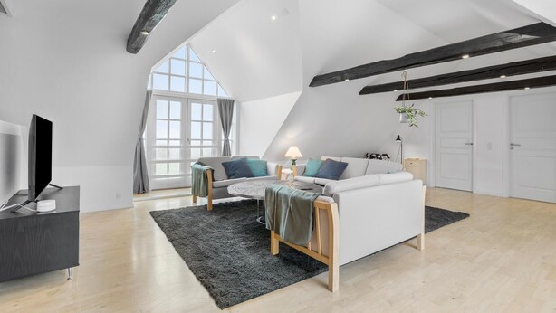 Un espacioso loft con techos altos, un ventanal grande, un sofá blanco, un televisor y un escritorio.