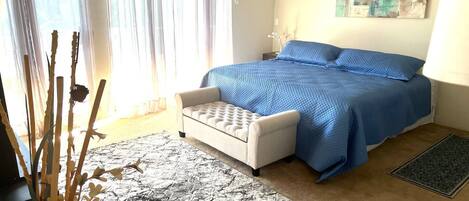 Een slaapkamer met een bed, een witte stoel, een vloerkleed en een schilderij aan de muur.