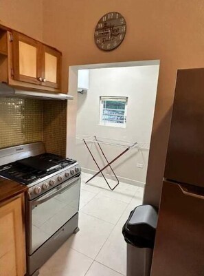 A kitchen with a stove, cabinets, a clock, and a window.