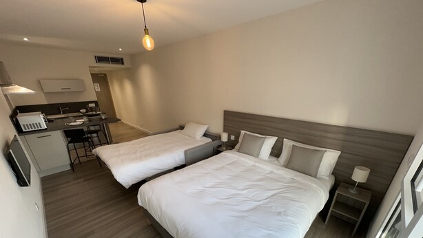 Een hotelkamer met twee bedden, een kitchenette en een klein eethoekje.