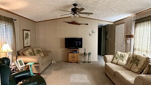 A living room with a ceiling fan, a TV, a sofa, a chair, and a small cabinet.