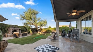 A patio area with a checkered mat, outdoor furniture, and a view of a tree and a stone structure. - PRIVATE RESORT RETREAT - Pool, Hot Tub, Sauna & Games (Gilbert)