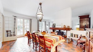 A dining area with a large table, chairs, and a hanging light fixture.