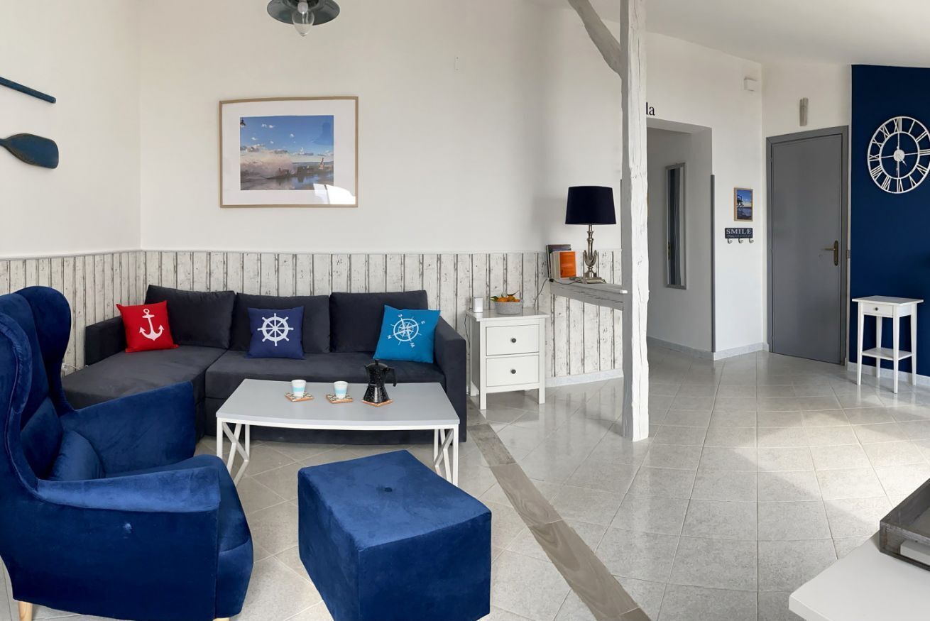 Un soggiorno moderno con un divano componibile, un tavolino da caffè e poltrone blu. In evidenza, un quadro appeso alla parete e un orologio sulla porta.