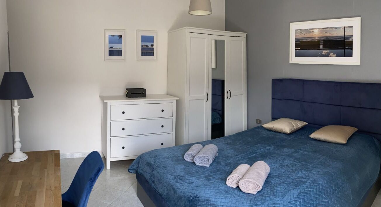 A bedroom with a bed, a wardrobe, a desk, and a chair.