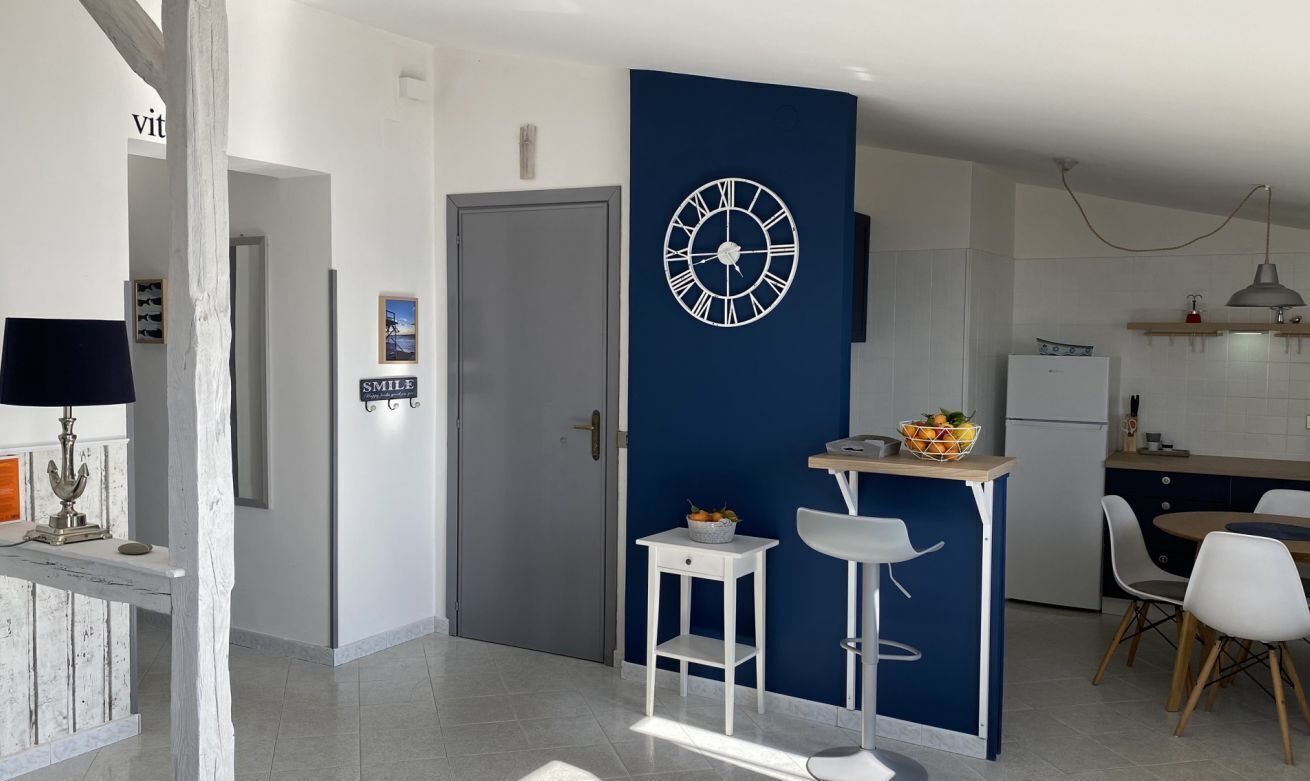 Una cucina moderna con una parete blu a contrasto, un orologio grande e un'area pranzo con sedie bianche.