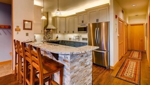 Una cocina con una isla central, taburetes de madera, electrodomésticos de acero inoxidable y salpicadero de azulejos.