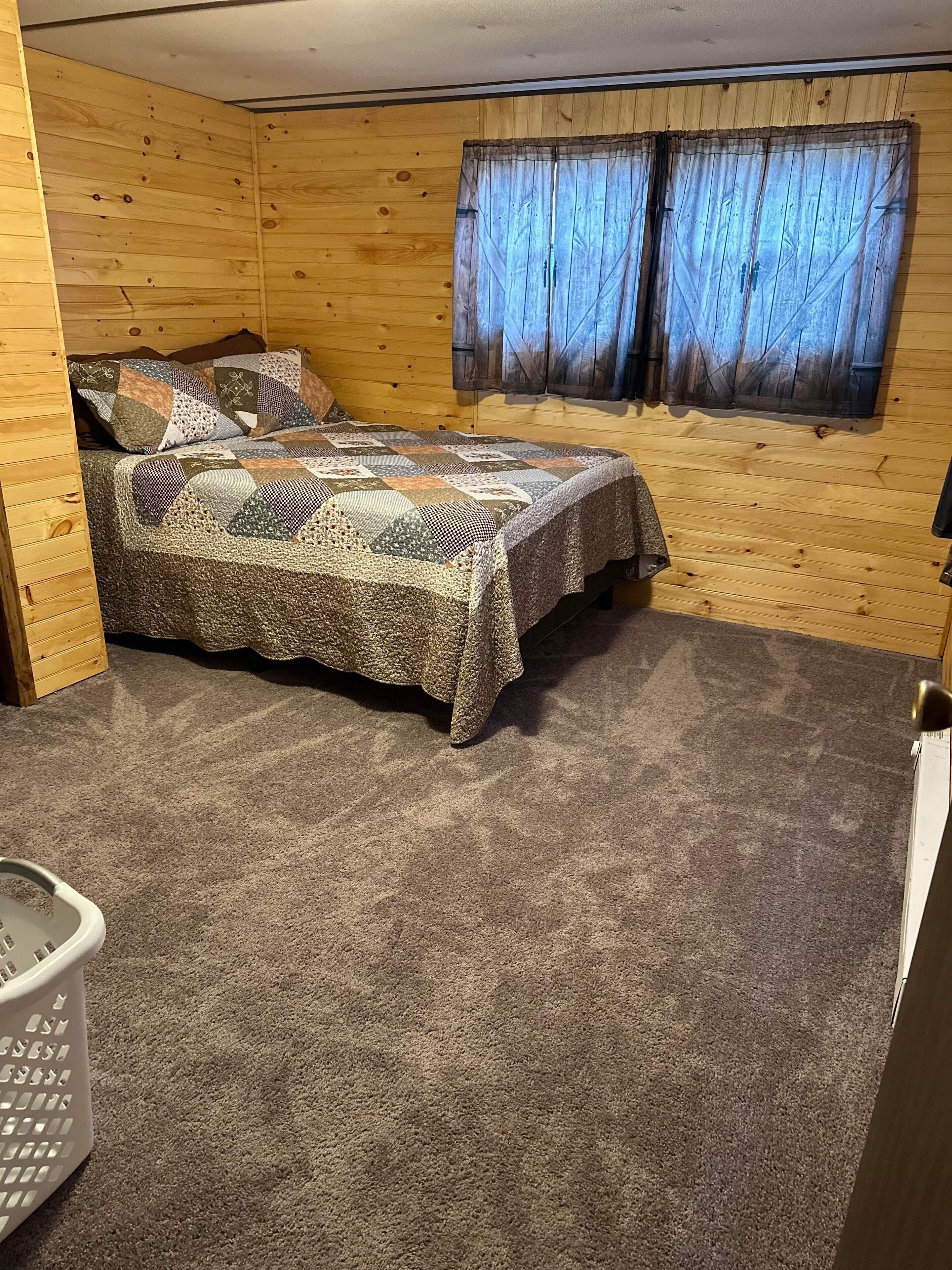 Une pièce chaleureuse avec un décor intérieur en bois, un lit recouvert d’une courtepointe à motifs et une fenêtre agrémentée de rideaux.