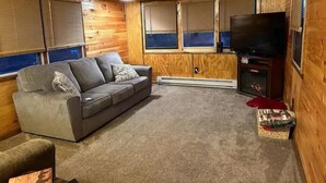 Una sala acogedora con un sofá gris, un televisor y paredes de madera.