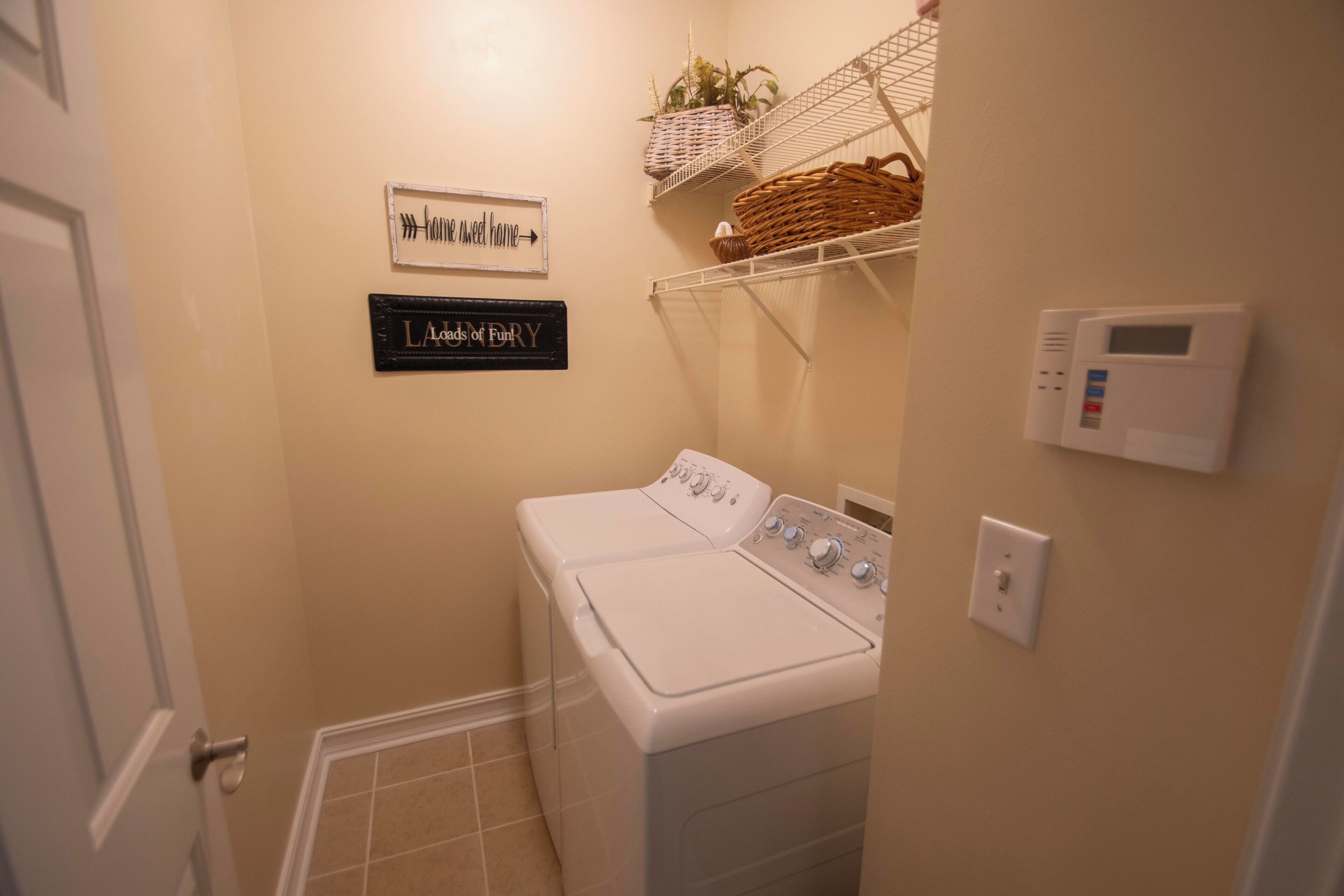 A laundry room with a washing machine, a wall-mounted thermostat, and two signs on the wall.