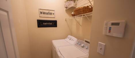 A laundry room with a washing machine, a wall-mounted thermostat, and two signs on the wall.
