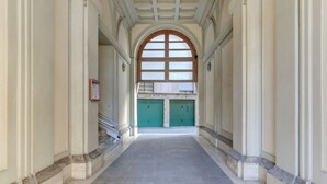 Um corredor com piso de azulejos, paredes brancas e uma porta verde no final.