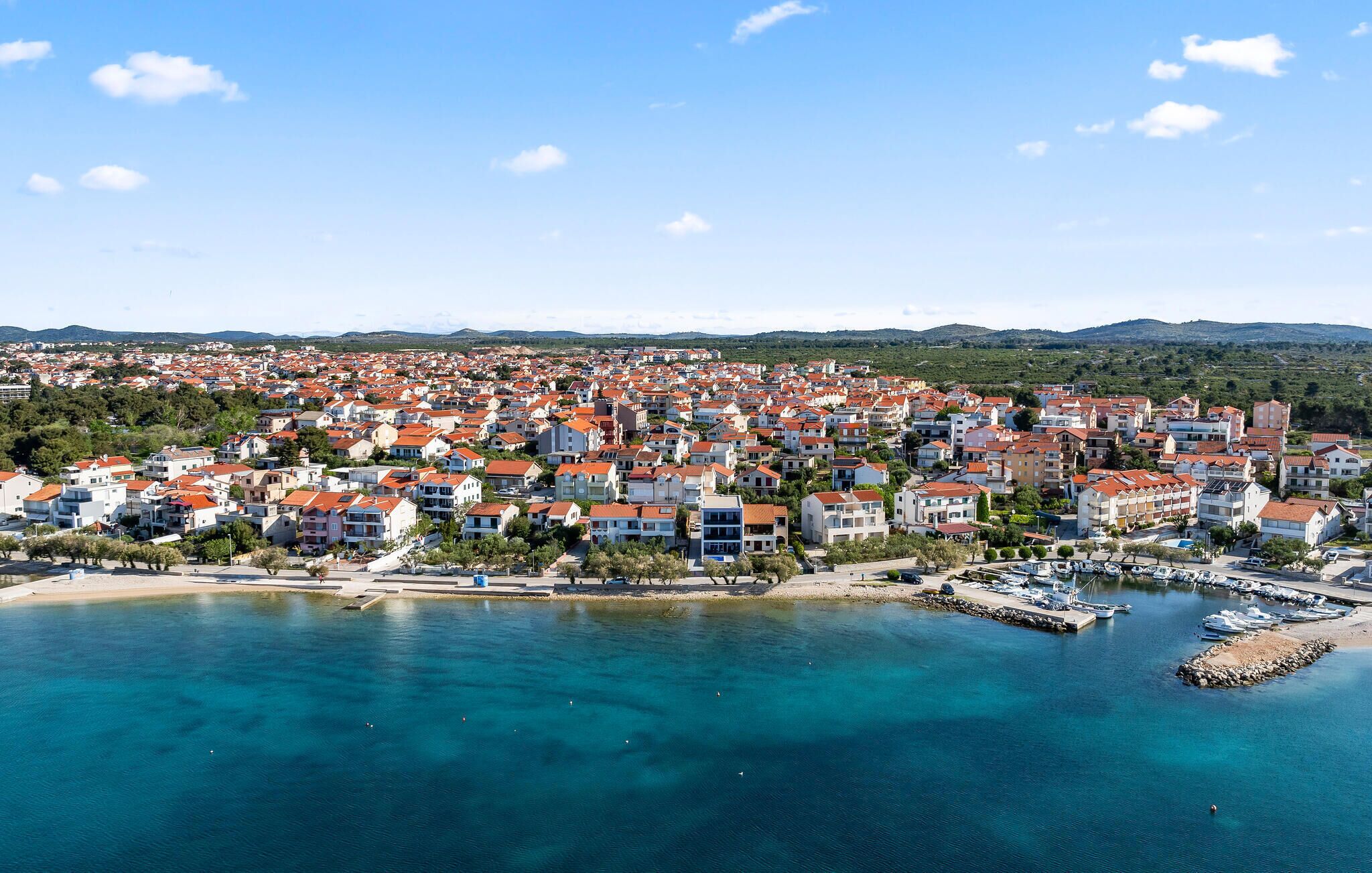 A coastal town with a marina, red-roofed buildings, and clear blue waters.