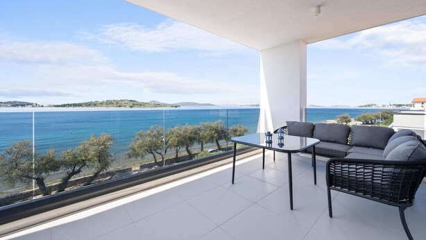 A balcony with a table and sofa, overlooking a body of water and distant land.
