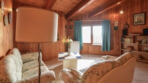 A cozy cabin interior with wooden walls, a large lamp, floral-patterned sofas, a small table with a vase of flowers, and a bookshelf. - 3 bedroom lovely home in San Giorgio (San Giorgio)