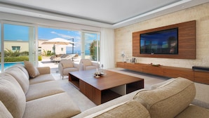 A modern living room with a large TV, comfortable seating, and a view of the pool and outdoors. - Beach front home in Savudrija (Savudrija)