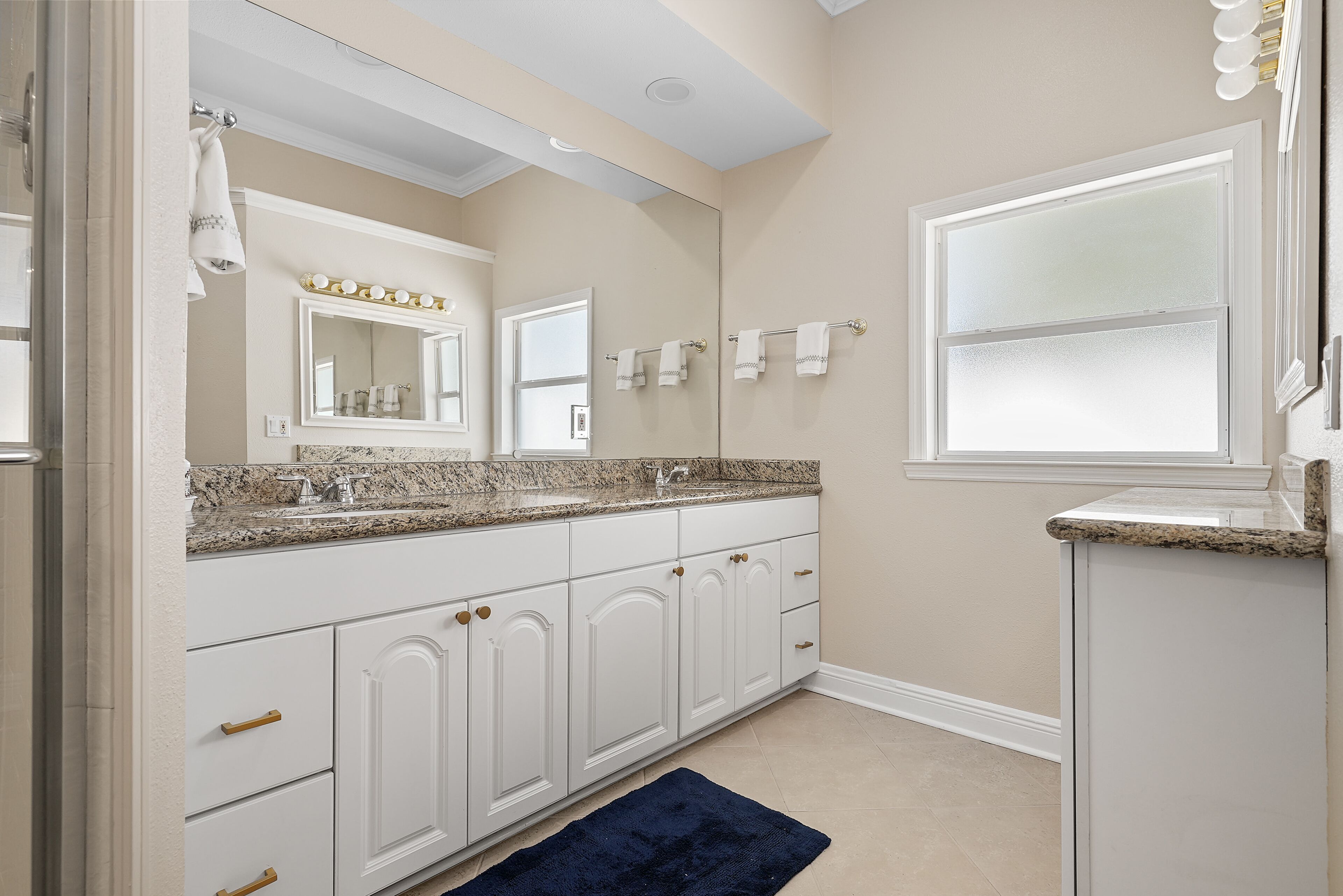 A bathroom with white cabinetry, a granite countertop, a large mirror, and a window.