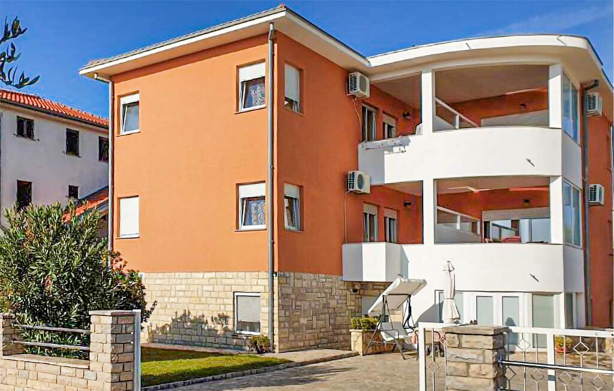 A multi-story apartment building with a flat roof, balconies, and a small garden area.