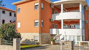 Un edificio de apartamentos de varios pisos con techo plano, balcones y un pequeño jardín.