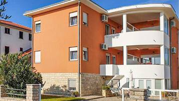 A multi-story apartment building with a flat roof, balconies, and a small garden area.