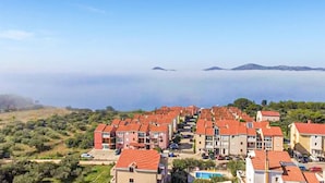 Zona residencial costera con casas escalonadas, vistas despejadas al mar y montañas en la distancia.