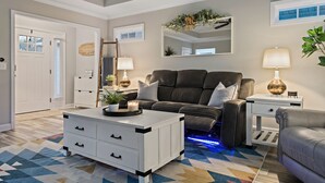 A modern living room with a sofa, a coffee table, and a side table. There is a mirror on the wall and a door leading to another room.