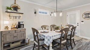 A dining area with a checkered tablecloth, wooden chairs, a coffee sign, a fireplace, and a chandelier.