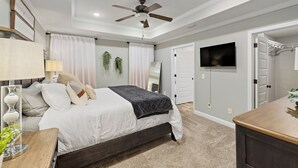 A bedroom with a bed, ceiling fan, TV, and a walk-in closet.