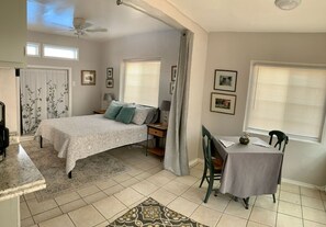 Une chambre à coucher avec un lit, un bureau et une chaise. Il y a des fenêtres avec des rideaux, un ventilateur de plafond et un tapis.