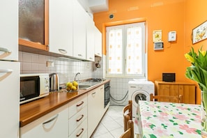 Une cuisine compacte avec des meubles blancs, un four à micro-ondes, un grille-pain et un lave-linge.