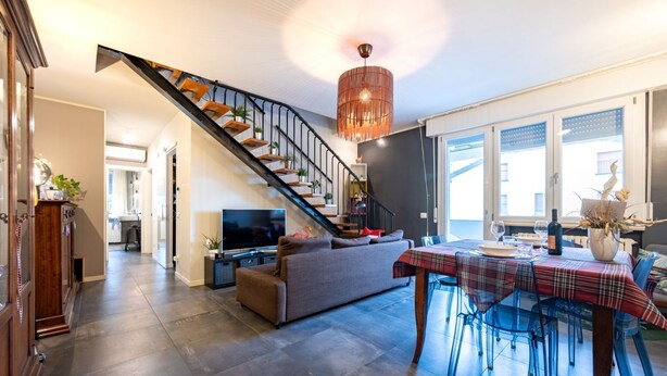 Ein modernes Wohnzimmer mit einer Couch, einem Esstisch mit Stühlen, einem Fernseher und einer Treppe mit Geländer.