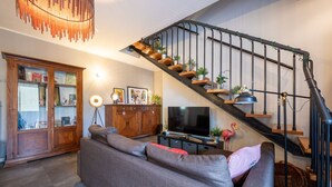 Ein Wohnzimmer mit einer Couch, einem Fernseher, einem Holzschrank und einer Treppe mit Pflanzen.