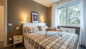 Ein Schlafzimmer mit Bett, Nachttischen, einem gerahmten Bild, einem Fenster mit Vorhängen und einem Heizkörper.