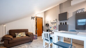 A modern living room with a brown sofa, white dining table, and a kitchen area with a microwave and shelves. - Comfortable attic located on the third and last floor of a building without a lift.It comfortably accommodates two people in 40 m2 of space with a double bedroom.Small building with a green space and ample free parking in front of the house, near the cen (Parma)