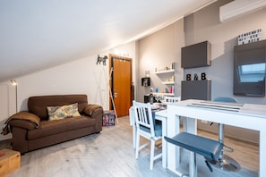 Un soggiorno moderno con un divano marrone, un tavolo da pranzo bianco e una zona cucina con forno a microonde e scaffali.