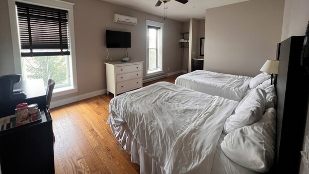 A bedroom with two beds, a ceiling fan, a TV on a dresser, and a window with blinds. - Full House booking of a history building close to the Dunes (Chesterton)