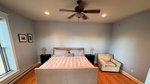 A bedroom with a large bed, two bedside tables, a ceiling fan, and a chair. - Full House booking of a history building close to the Dunes (Chesterton)