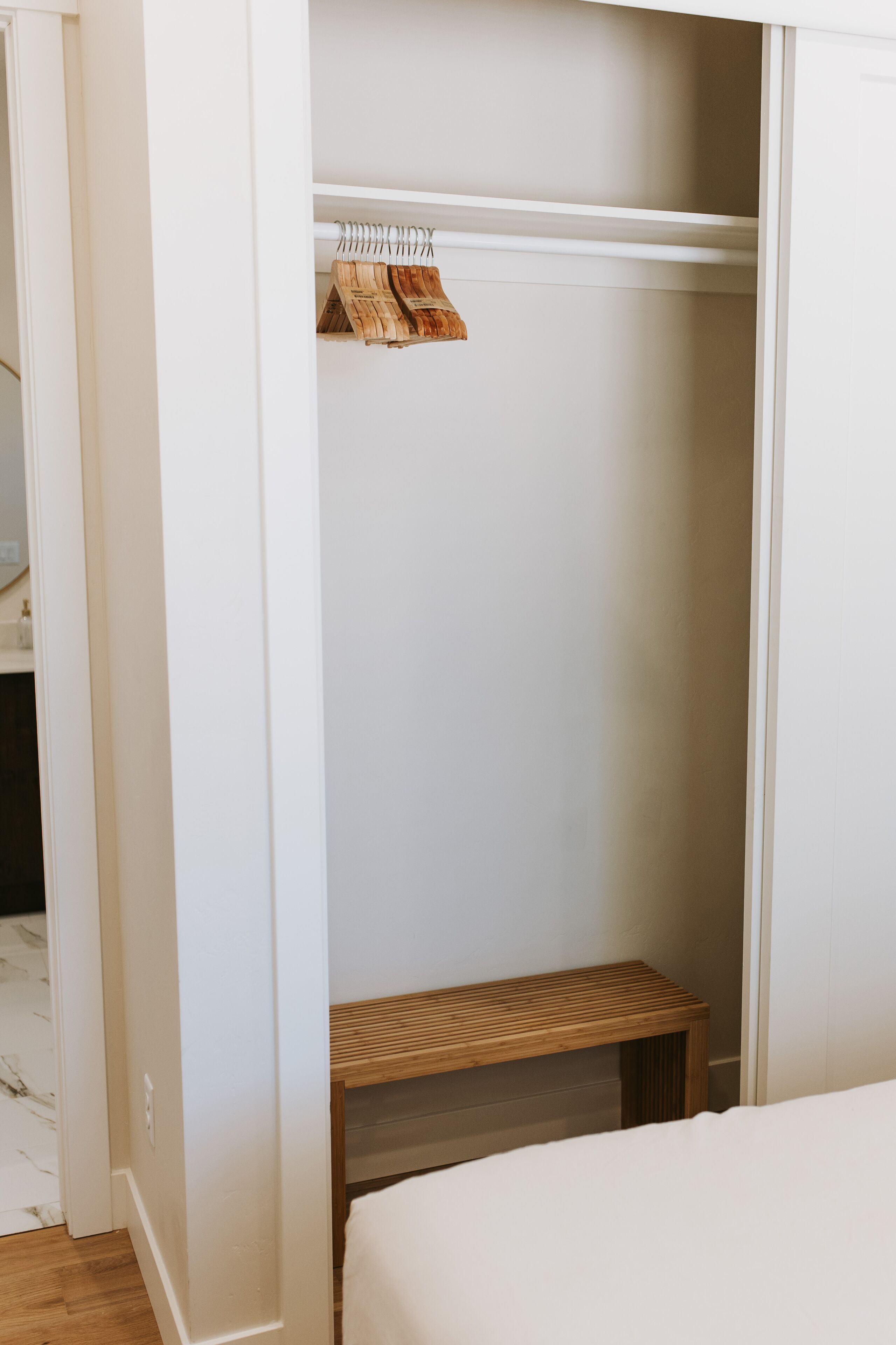Ein begehbarer Kleiderschrank mit einer hölzernen Sitzbank und Kleiderhaken.