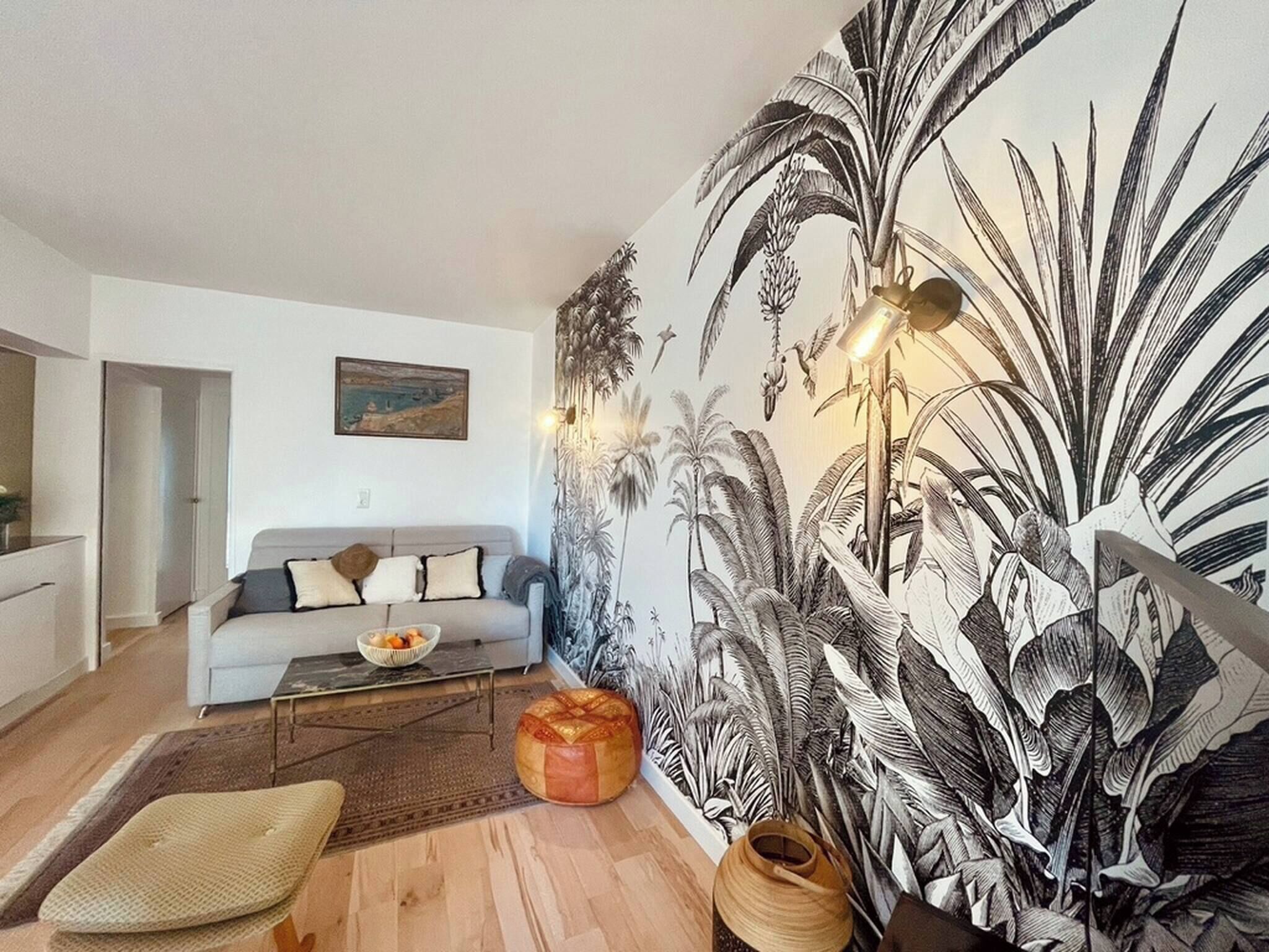 Un salon comprenant un canapé, une table basse, un tapis, une fresque murale et une lampe.