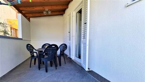 Eine überdachte Terrasse mit Tisch und Stühlen, einer Holzbalkendecke und einer weißen Wand mit einer Tür.
