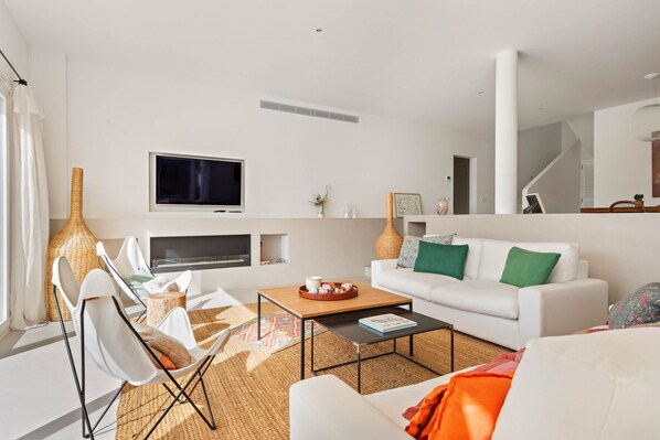 A modern living room with a white sofa, a coffee table, a TV, and a large window with curtains. - Villa Estrella - Canutells (Es Canutells)