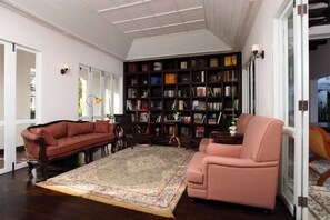 Un salón amplio con una gran estantería, un sofá rojo, un sillón rosa y una alfombra estampada.