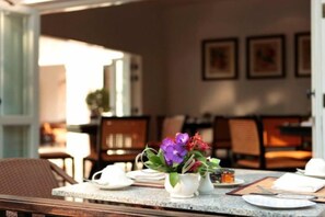 Un comedor con una mesa preparada para dos personas, que incluye un jarrón con flores, una taza y un plato.