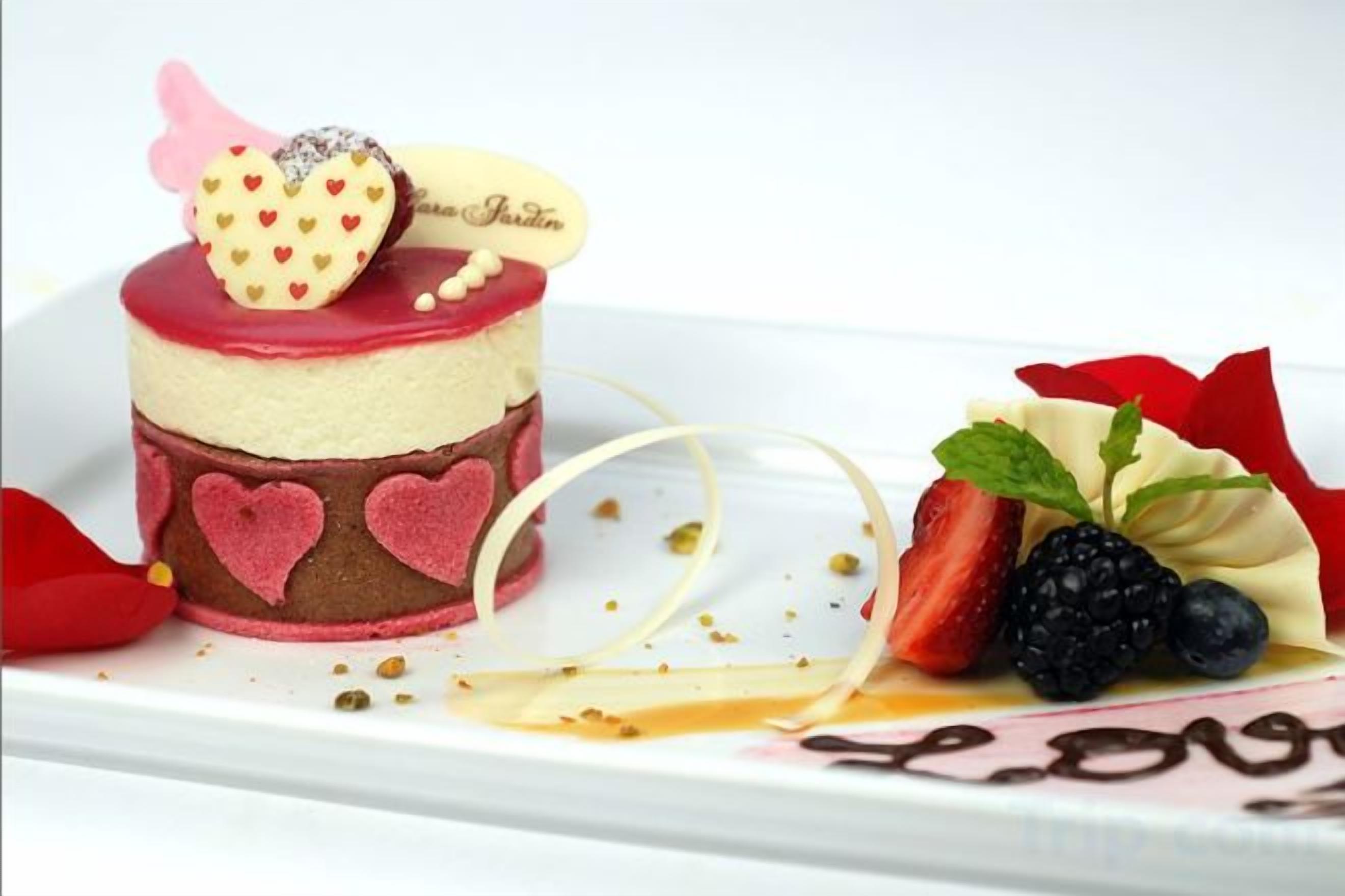 A dessert with a heart-shaped decoration on top, strawberries, and a small chocolate piece.